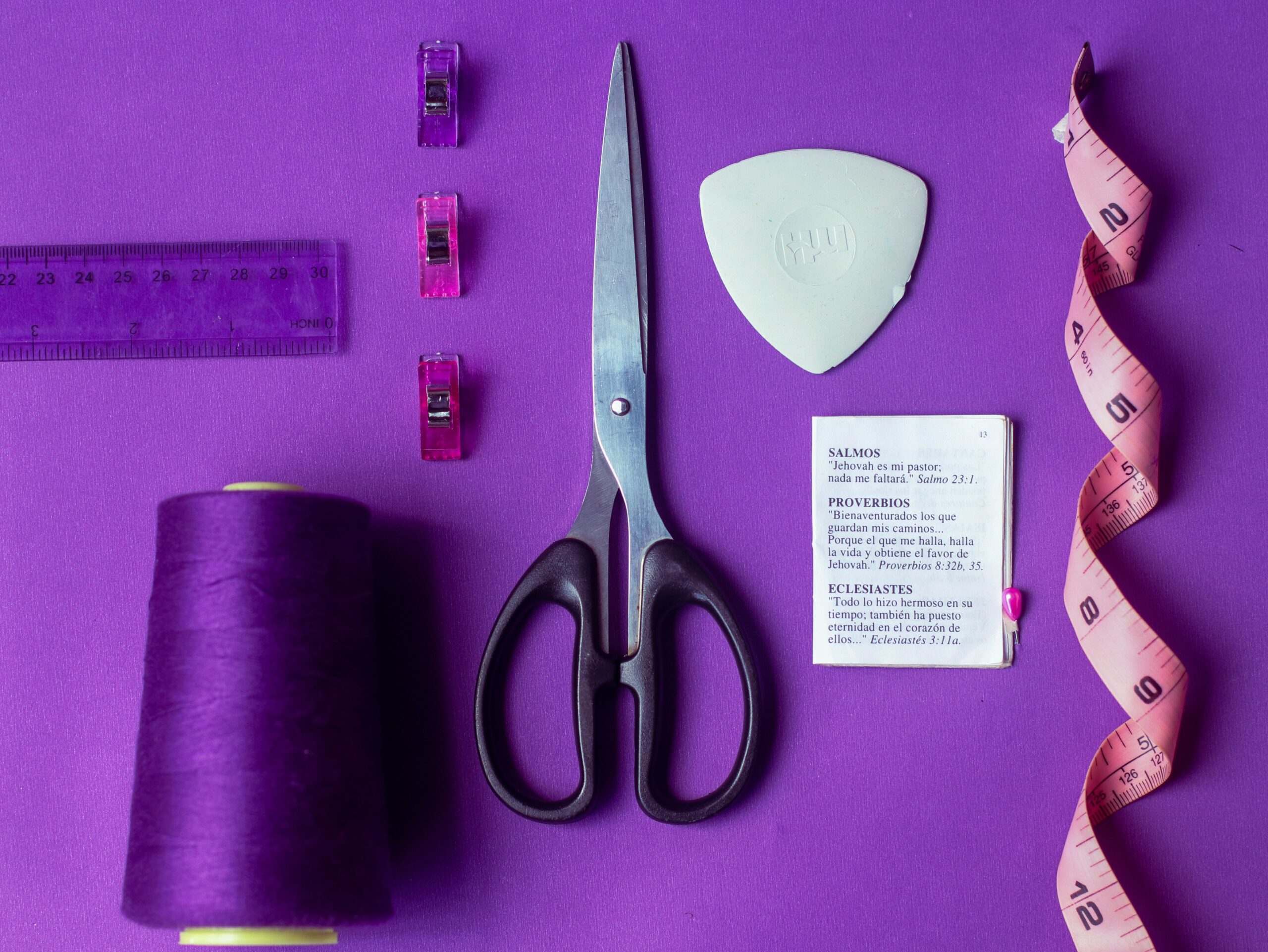 Flat lay of sewing tools including scissors, thread, and tape measure on a vibrant purple background.
